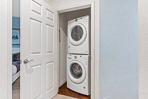 A laundry room with a front-loading washer and dryer, a door leading to a bedroom, and a carpeted floor. - 4BR West Lucaya Home Near Disney (Kissimmee)