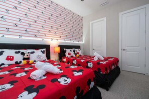 A hotel room with three beds, each with a Mickey Mouse themed bedspread. There is a wall with a Mickey Mouse pattern and a door visible. - 4BR Disney-themed Townhome (Kissimmee)