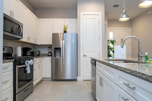 A modern kitchen with white cabinets, stainless steel appliances, a granite countertop, and a built-in dishwasher. - 4BR Disney-themed Townhome (Kissimmee)