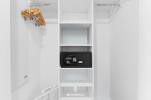 A white interior with a digital safe on the lower shelf and a clothes rack with wooden hangers on the upper shelf. - Bright Pininfarina Studio w/ Private Balcony (Hallandale Beach)