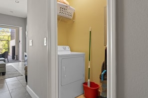 Ein Waschraum mit Waschmaschine, einem Wischmopp und einem Wäschekorb an der Wand.