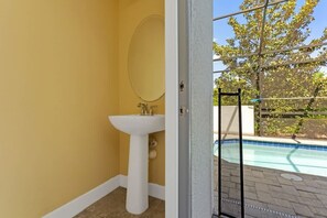 Ein Badezimmer mit weißem Waschbecken und Spiegel, Blick auf einen Pool im Freien.