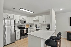 Una cocina moderna con armarios blancos, electrodomésticos de acero inoxidable y una isla central con taburetes de bar.