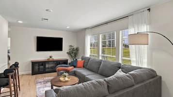A modern living room with a grey sofa, a flat-screen TV mounted on the wall, a wooden coffee table, and a floor lamp.