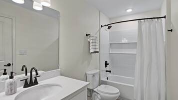Un bagno moderno con lavandino bianco, rubinetto nero, water bianco e zona doccia con tenda bianca.