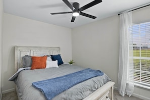 Ein Schlafzimmer mit einem Bett, einem Deckenventilator, einem Fenster mit Jalousien und Blick ins Freie.
