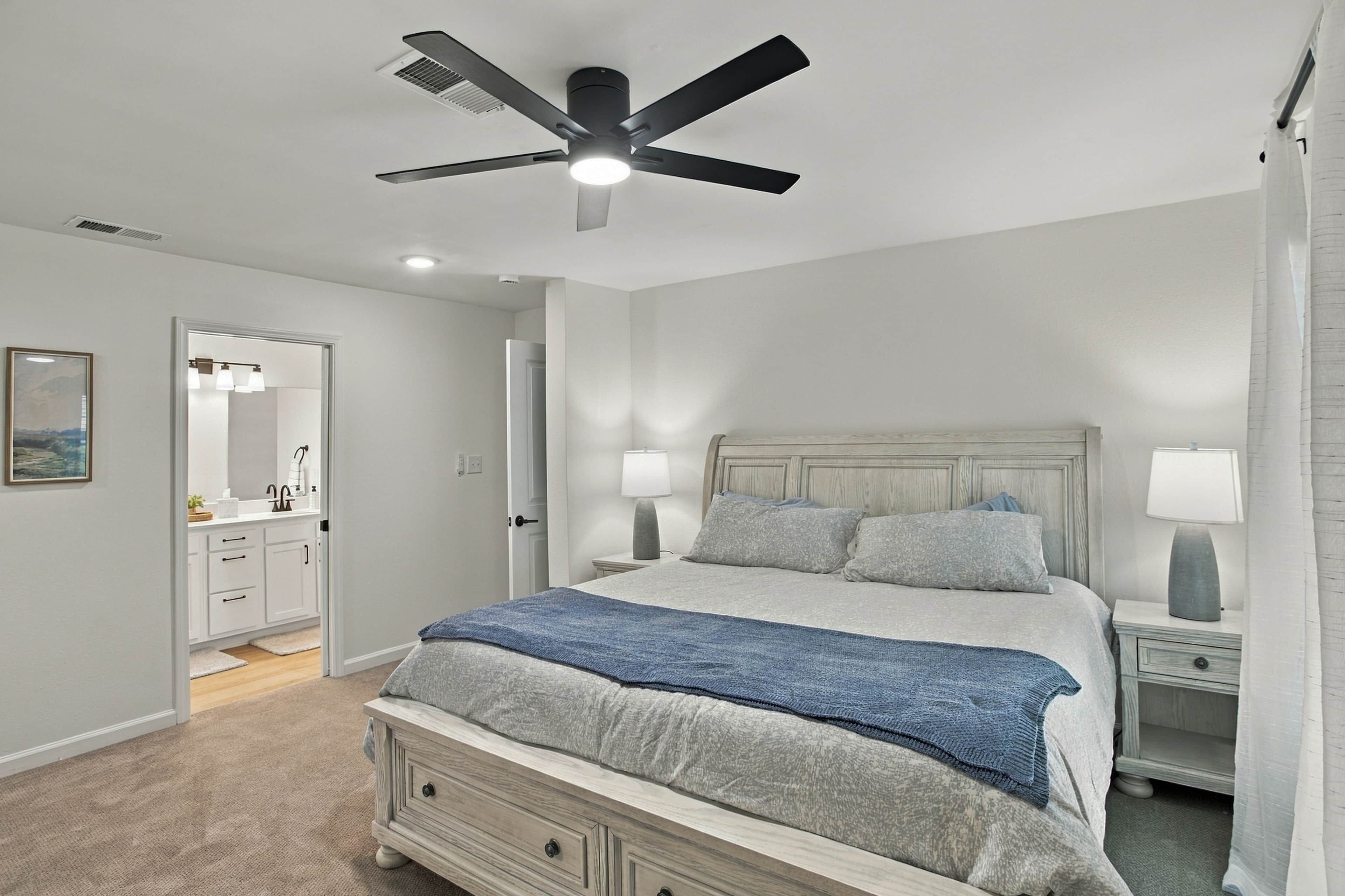 Un dormitorio con cama, dos mesitas de noche, ventilador de techo y mesita con lámpara.