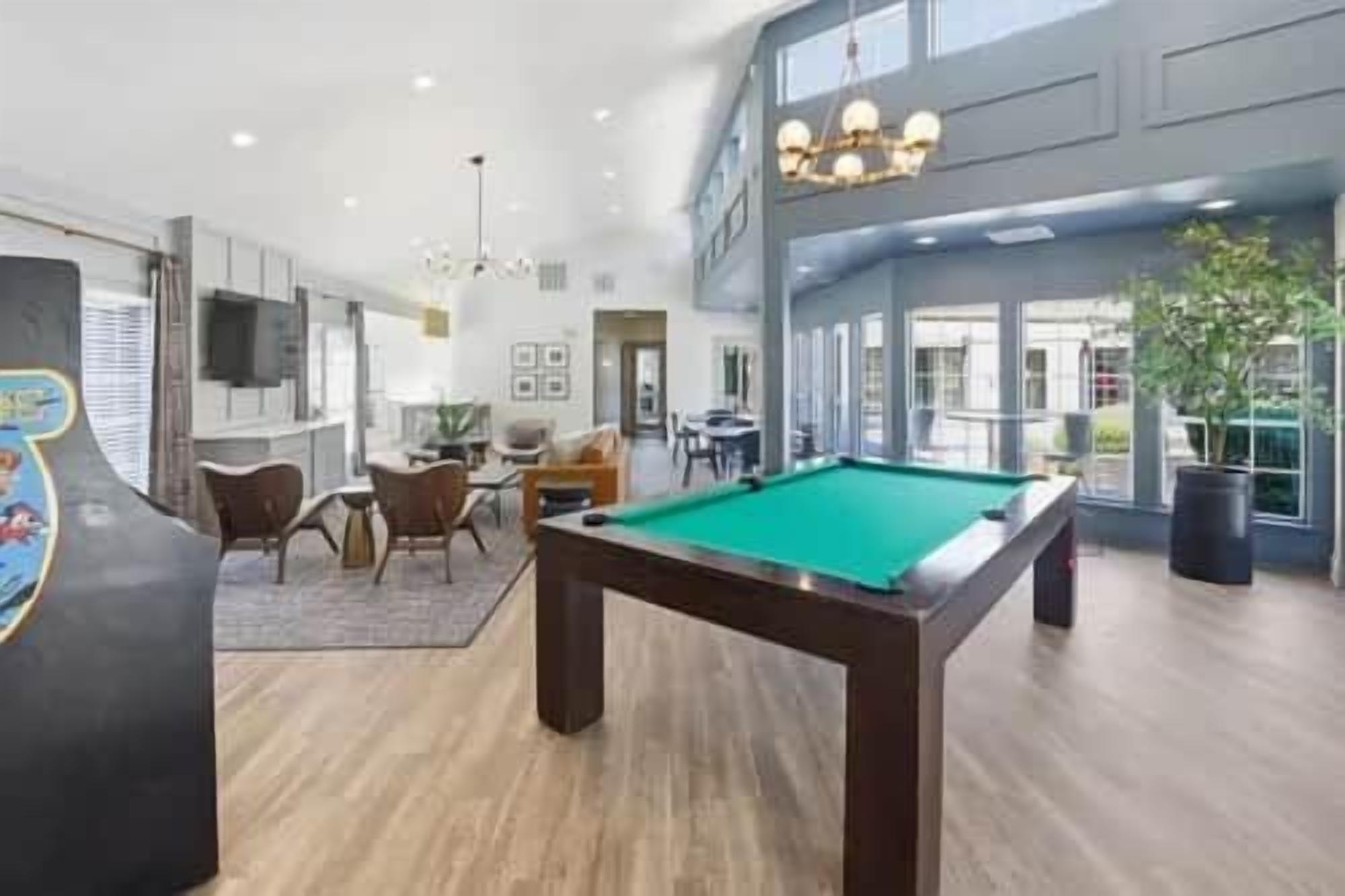A pool table in a spacious room with a high ceiling and modern lighting fixtures.