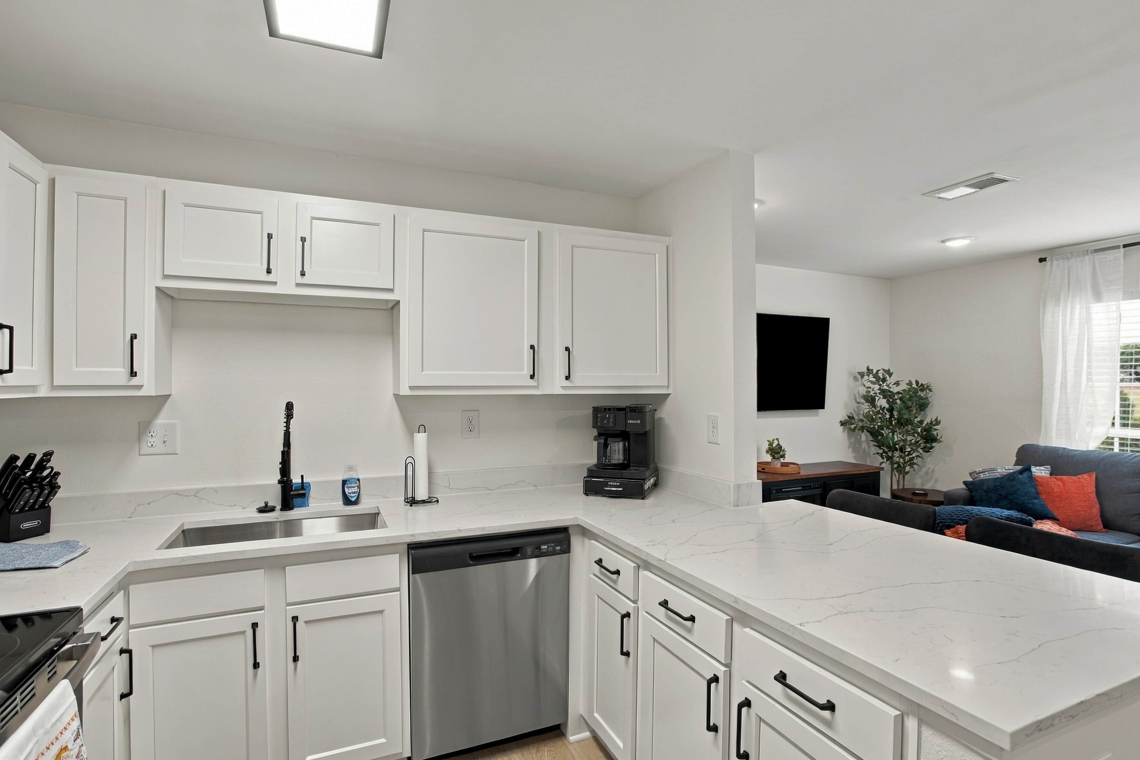 A modern kitchen with white cabinets, a dishwasher, and a coffee maker.