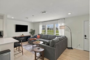 Ein modernes Wohnzimmer mit einem grauen Sofa, einem Couchtisch und einem an der Wand befestigten Fernseher.