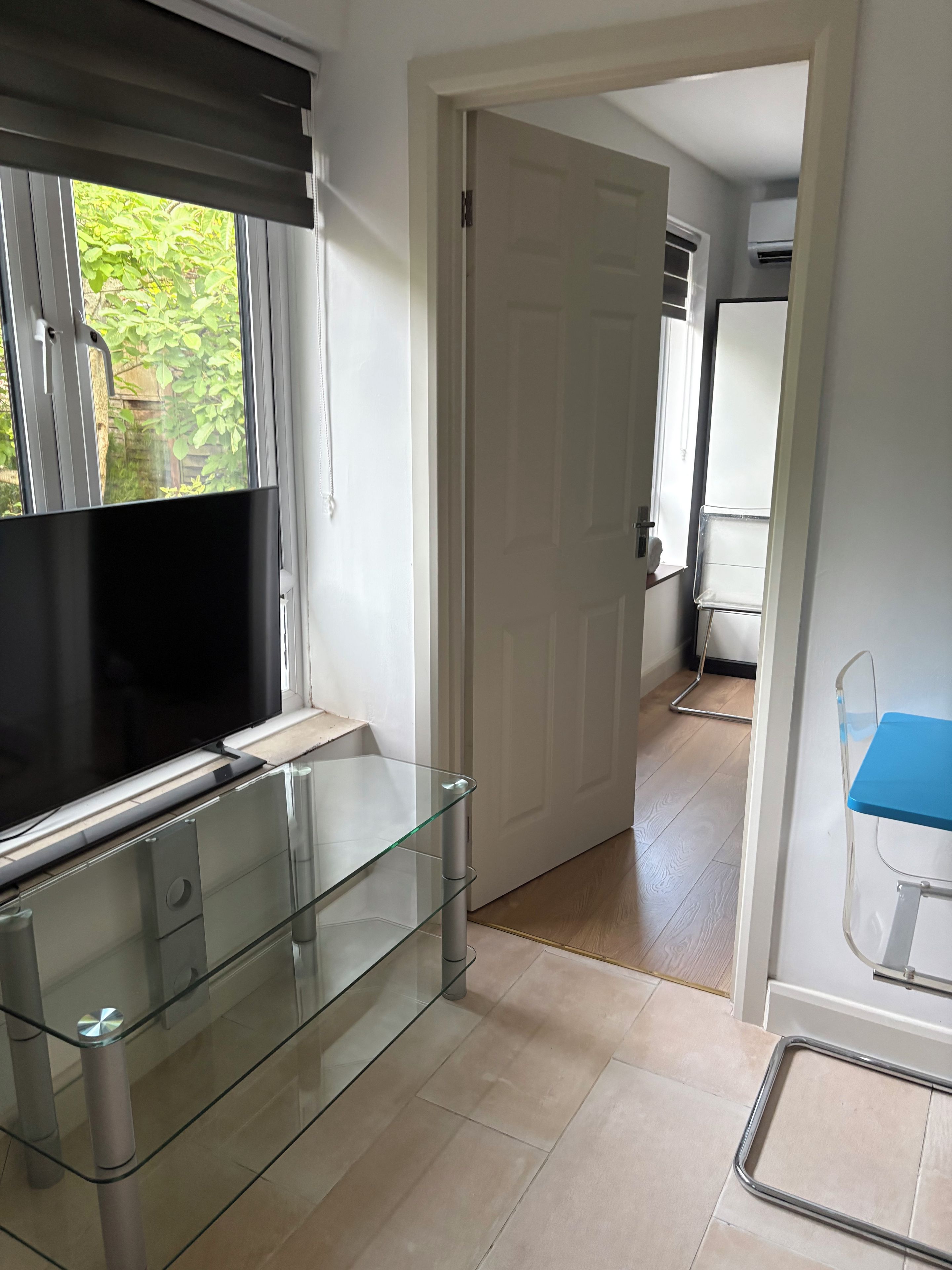 A modern kitchen with a flat-screen TV, glass shelving, and a door leading to another room.