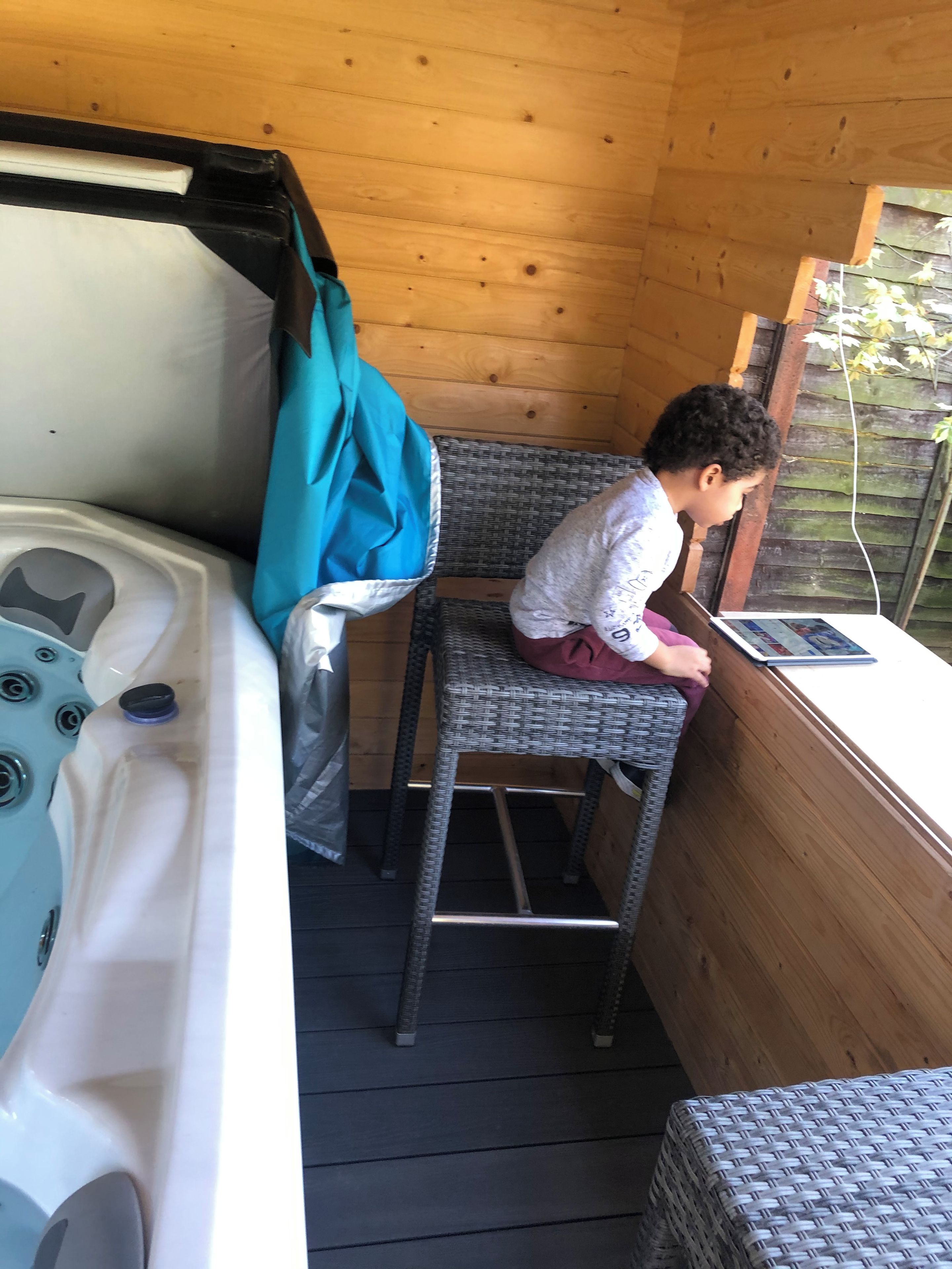 A wooden cabin interior with a hot tub, a wicker chair, and a laptop on a wooden table.
