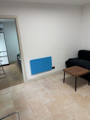 A room with a black sofa, a wooden coffee table, a blue radiator, and a tiled floor.