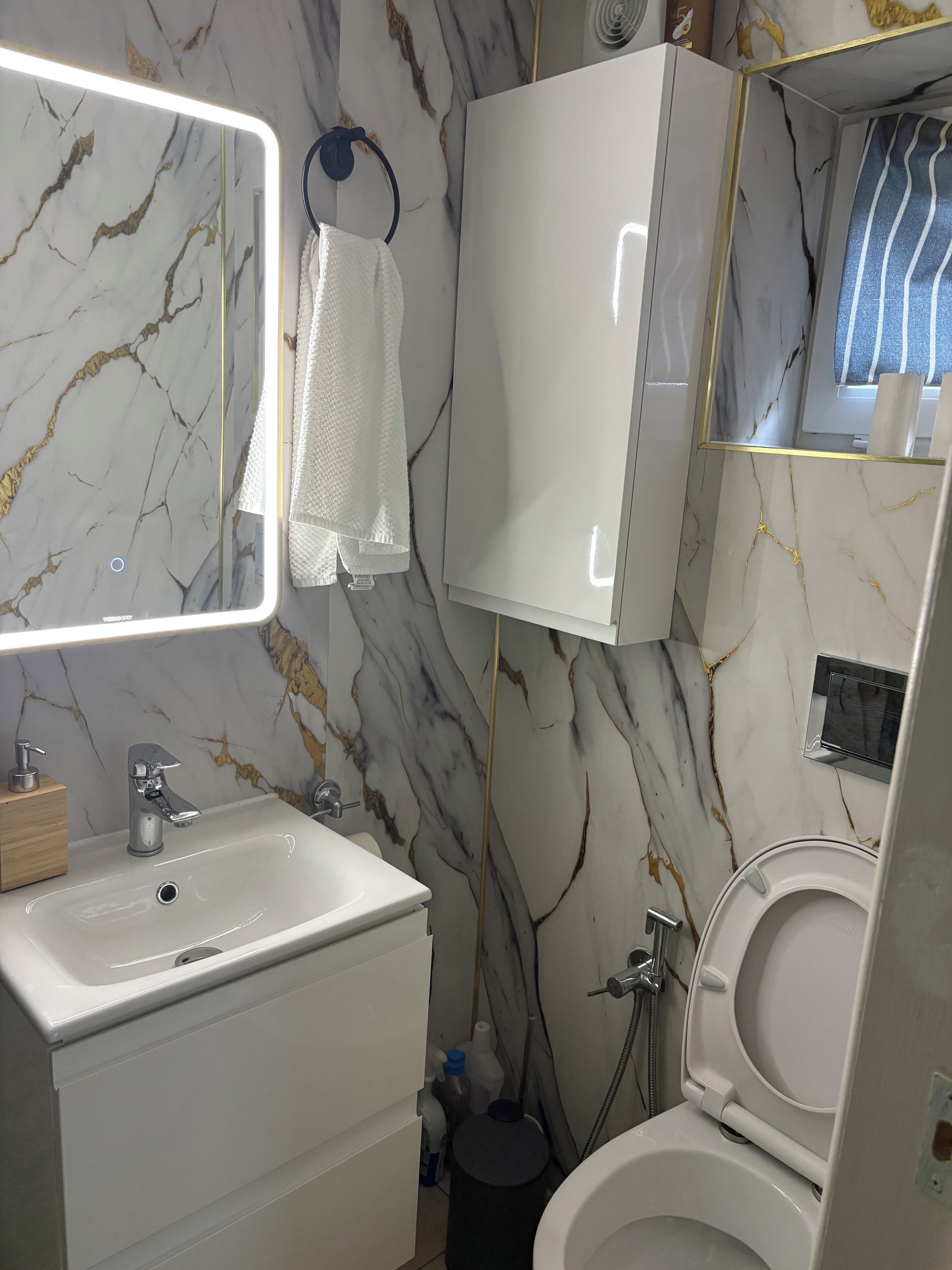 A bathroom with a marble backsplash, a white sink, a mirror, a towel, and a toilet.