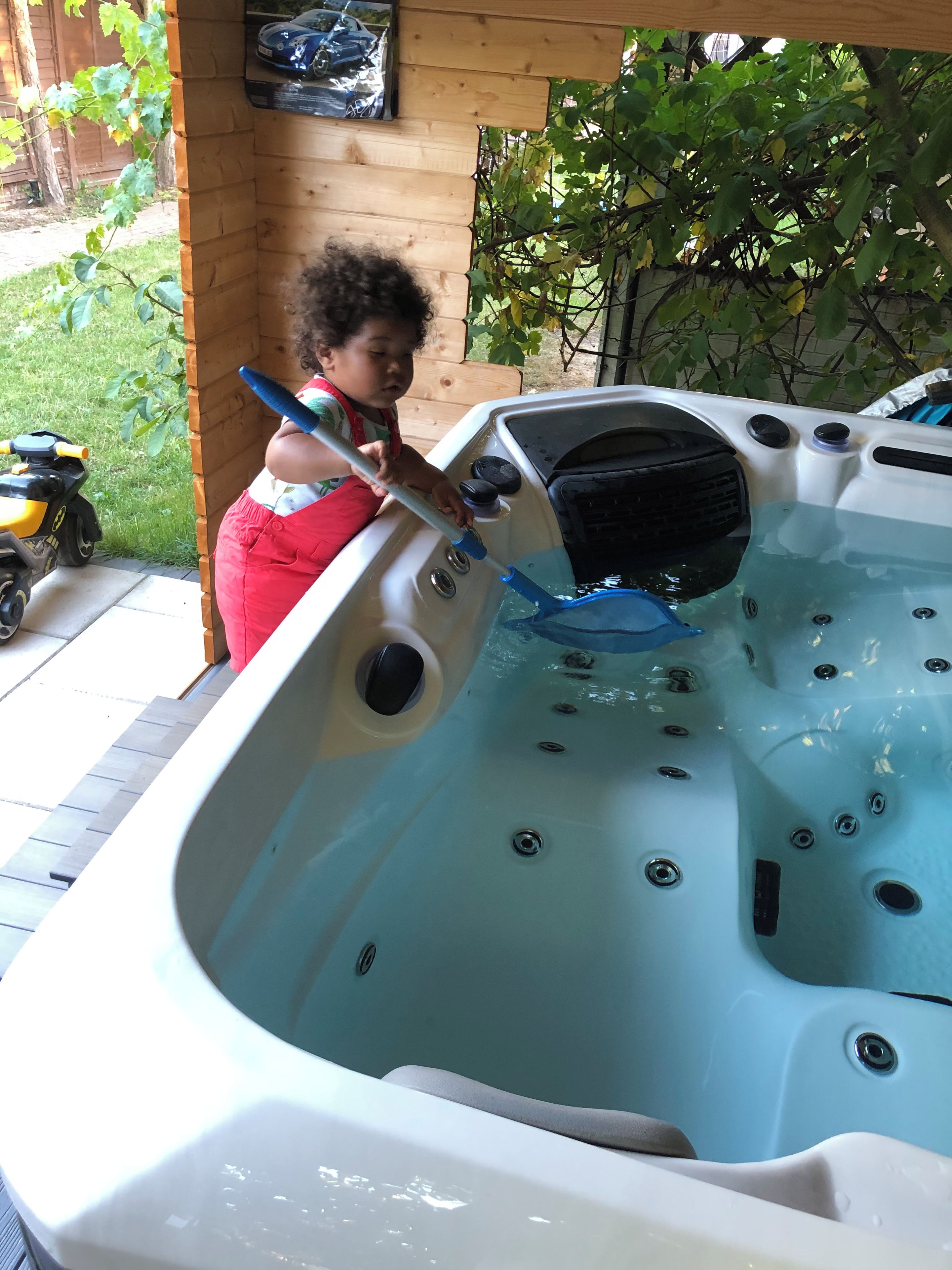 A hot tub with a wooden deck and a child playing with a toy.