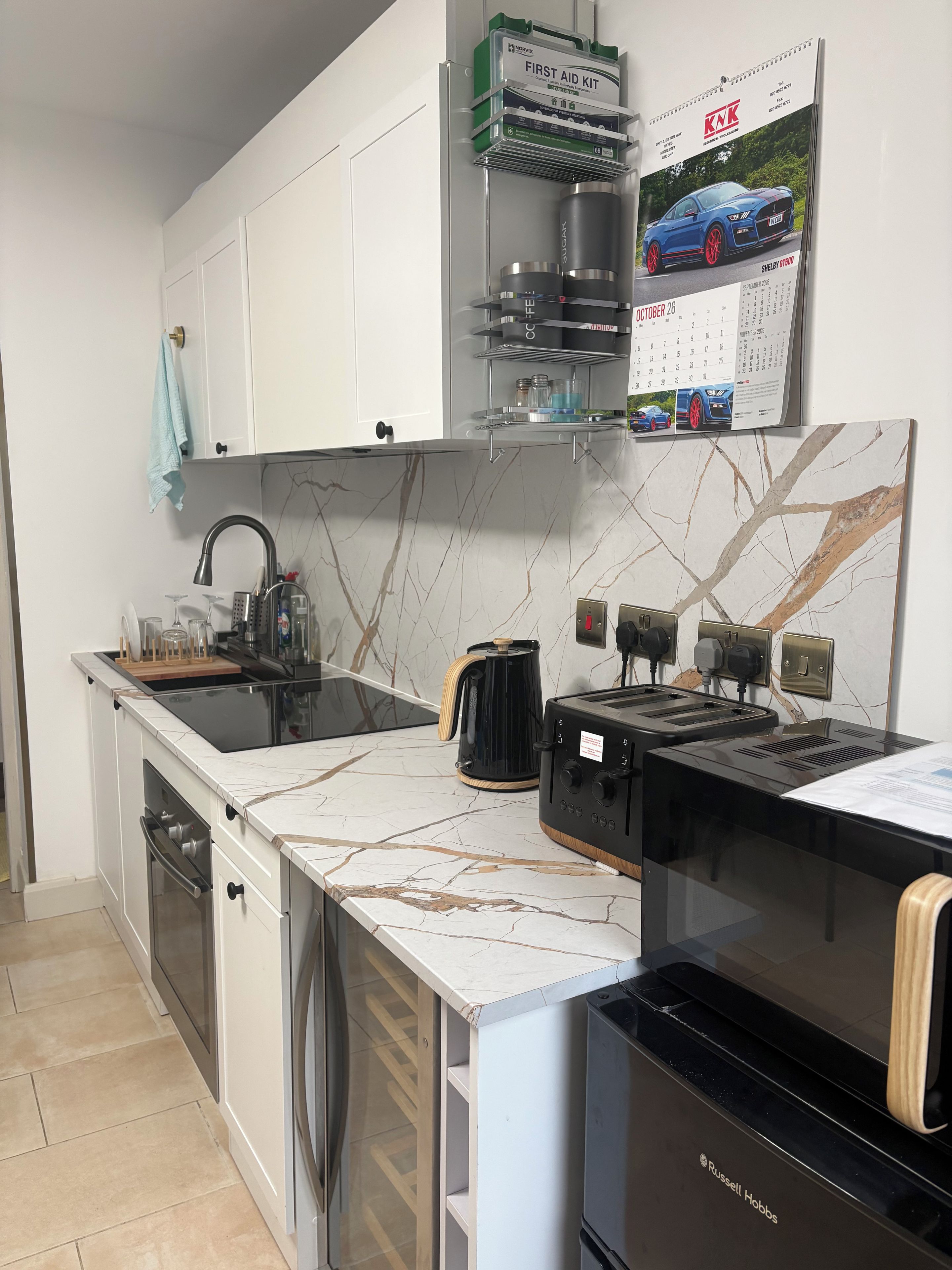 A modern kitchen with a marble countertop, a black Russell Hobbs toaster, a coffee maker, and a calendar with a car image.