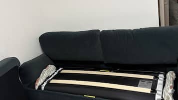 A black sofa with a mattress and pillows, a tiled floor, and a door leading to another room.