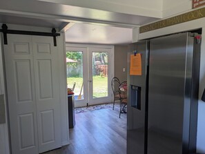 A kitchen with a stainless steel refrigerator, a white door, and a view into a backyard through a glass door. - Cozy 2-bdrm house in Cottage Grove with Fenced Yard, Plenty of Parking (Cottage Grove)