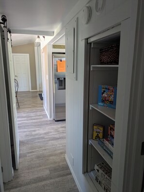 Un pasillo con una puerta blanca, un dispensador de agua y una estantería con juegos de mesa.