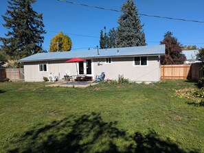 Une maison de plain-pied avec un patio, un parasol rouge et une cour arrière clôturée.