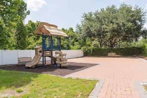 A playground with a slide and climbing structure, surrounded by a brick pathway and greenery. - Modern 4BR Home in Lucaya Village Kissimmee (Kissimmee)
