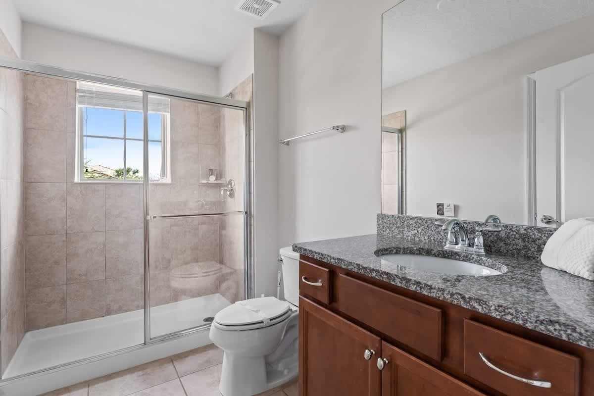 A modern bathroom with a glass shower enclosure, a white toilet, a granite countertop sink, and wooden cabinets.
