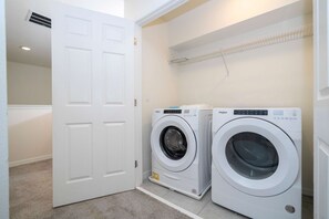 A laundry room with two front-loading washing machines, a white door, and a ceiling vent. - Themed 4BR Townhome w/ Pool at Solara (Kissimmee)