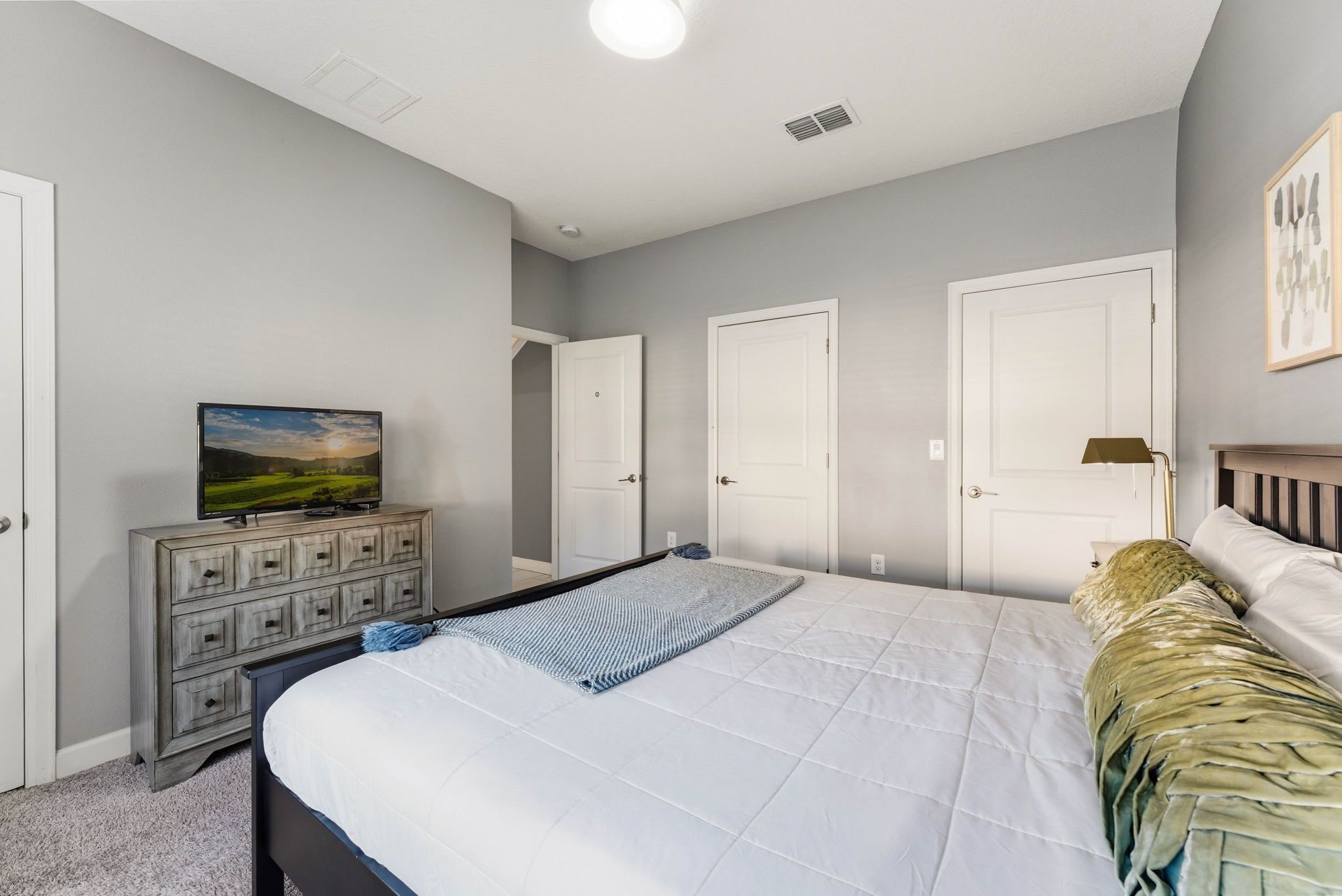 A bedroom with a bed, dresser, and a television on a stand.