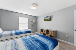A bedroom with two beds, a nightstand, a shelf with storage boxes, and a wall-mounted TV. - 4BR Townhome w/ Pool at Champions Gate (Davenport)