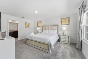A bedroom with a bed, bedside tables, a nightstand, a dresser, and a mirror. - Solara 4BR w/ Private Pool Near Disney (Kissimmee)