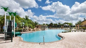 A swimming pool with a waterfall feature, palm trees, and a brick walkway. - 4BR Home w/ Pool at Paradise Palms Near Disney (Kissimmee)