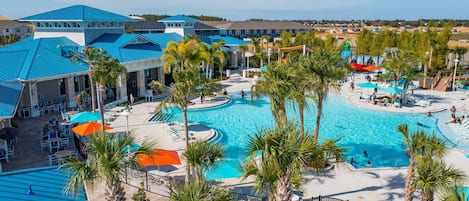 Un resort con una amplia piscina central, palmeras y un edificio de techo azul.