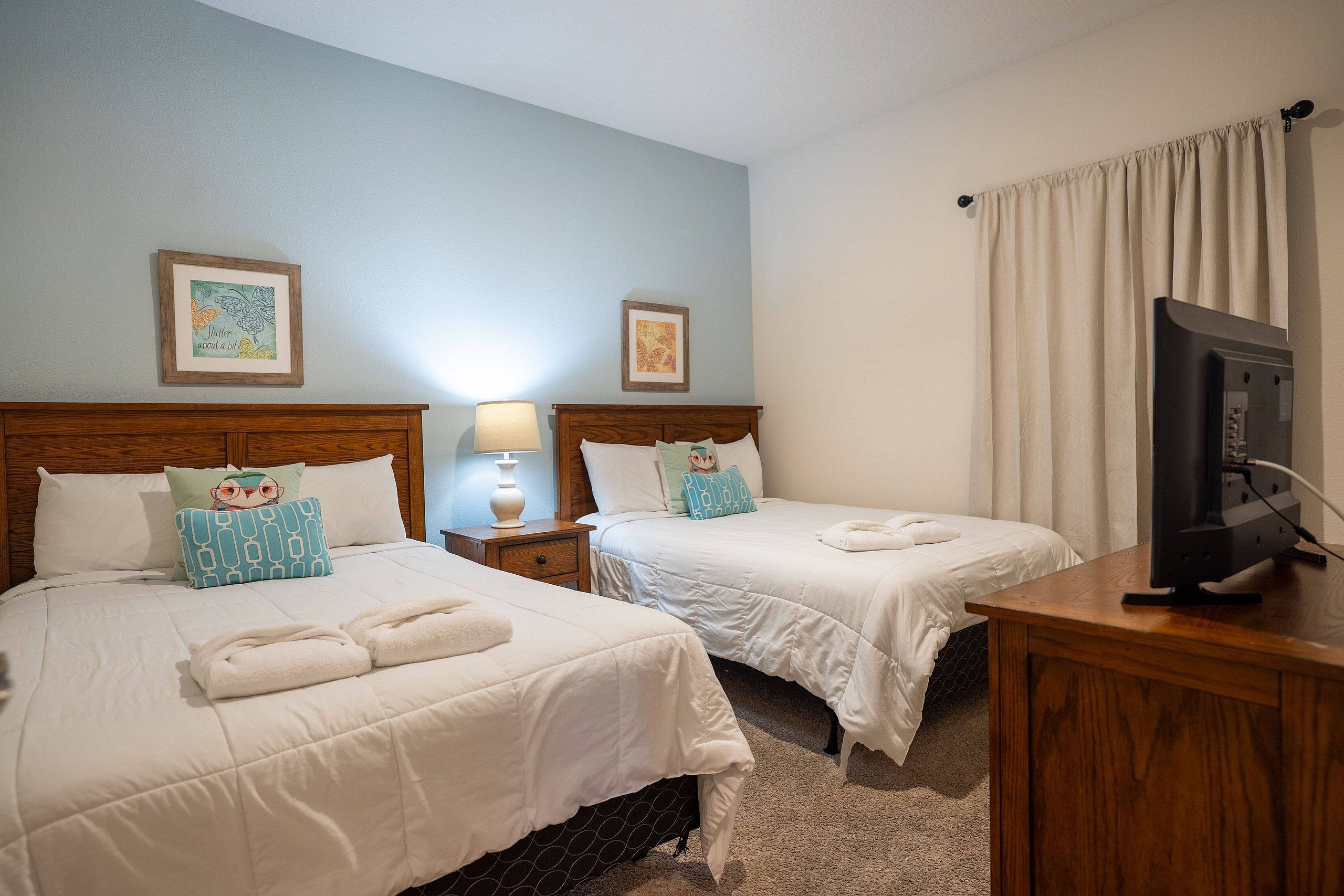 A hotel room with two beds, a TV, a lamp, and artwork on the walls.