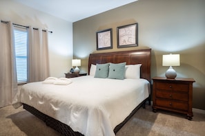 A neatly made bed with a headboard, two bedside tables with lamps, and a window with curtains. - 4BR Resort Home 10min From Disney (Kissimmee)