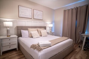 Ein ordentlich eingerichtetes Schlafzimmer mit einem großen Bett, zwei Nachttischen mit Lampen, einem Schreibtisch und einem Stuhl.