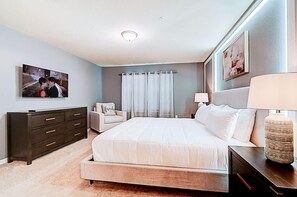 Ein Schlafzimmer mit einem großen Bett, einem Schminktisch, einem Sessel, einem Fernseher und einer Lampe.