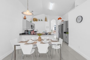 A modern kitchen with white cabinetry, a dining table set for four, and a clock on the wall. - 4-bedroom House With Private Pool and spa (Kissimmee)