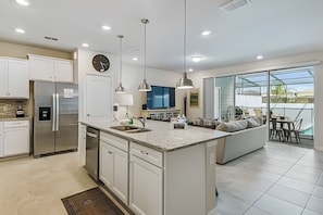 A modern kitchen with a central island, stainless steel appliances, pendant lighting, and a large window overlooking a patio area. - 5BR Solterra Townhome, Private Pool (Davenport)