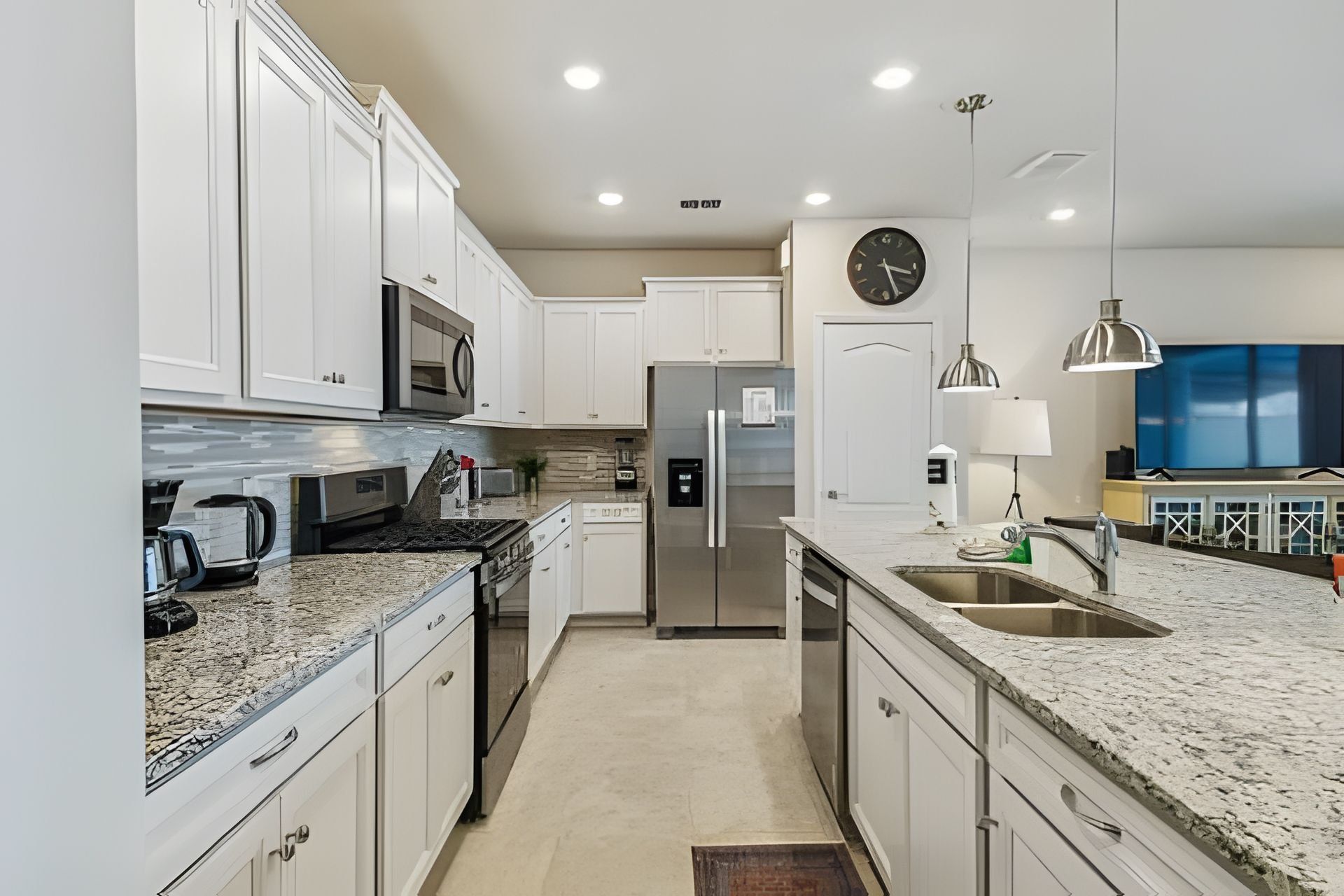 A modern kitchen with white cabinetry, stainless steel appliances, a granite countertop, and a built-in oven.