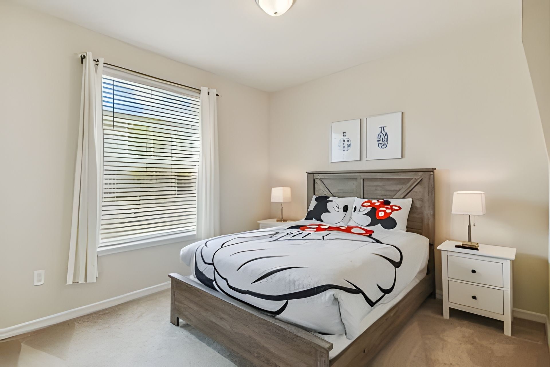 A bedroom with a bed, bedside tables, a window with blinds, and two wall-mounted artworks.