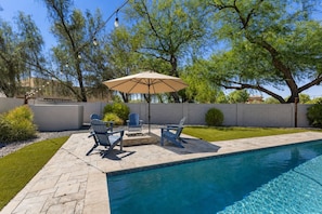 Ein Schwimmbad mit Terrassenbereich, Gartenmöbeln und einem großen Baum.