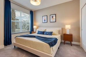 Ein Schlafzimmer mit einem großen Bett, zwei Nachttischen, einem Fenster mit Vorhängen und zwei gerahmten Bildern an der Wand.