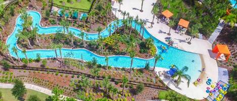 Vista aérea de un resort con piscina serpenteante, palmeras y zonas de descanso.