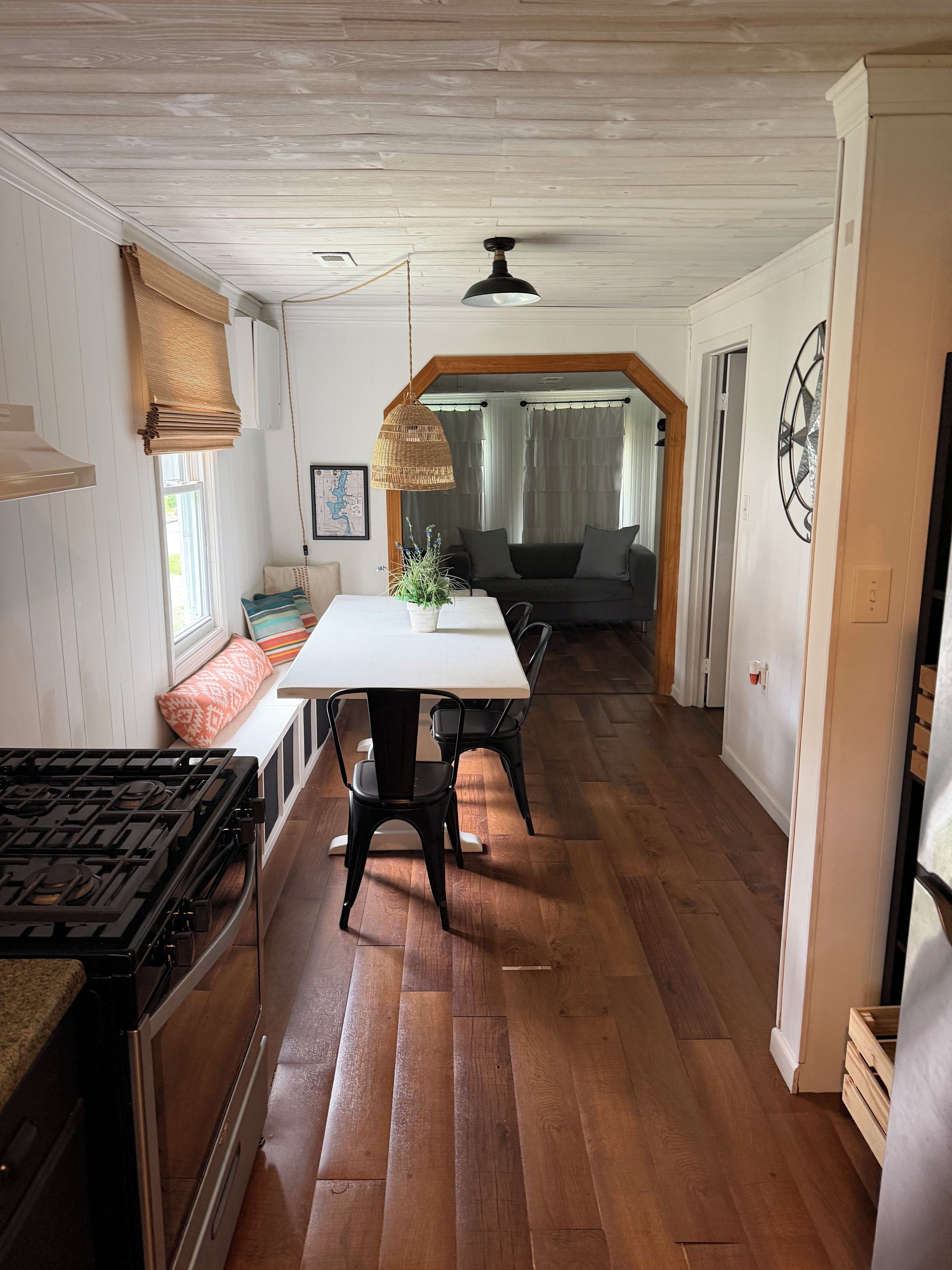 A kitchen with a stove, a dining table with chairs, a sofa, and a hanging light fixture.