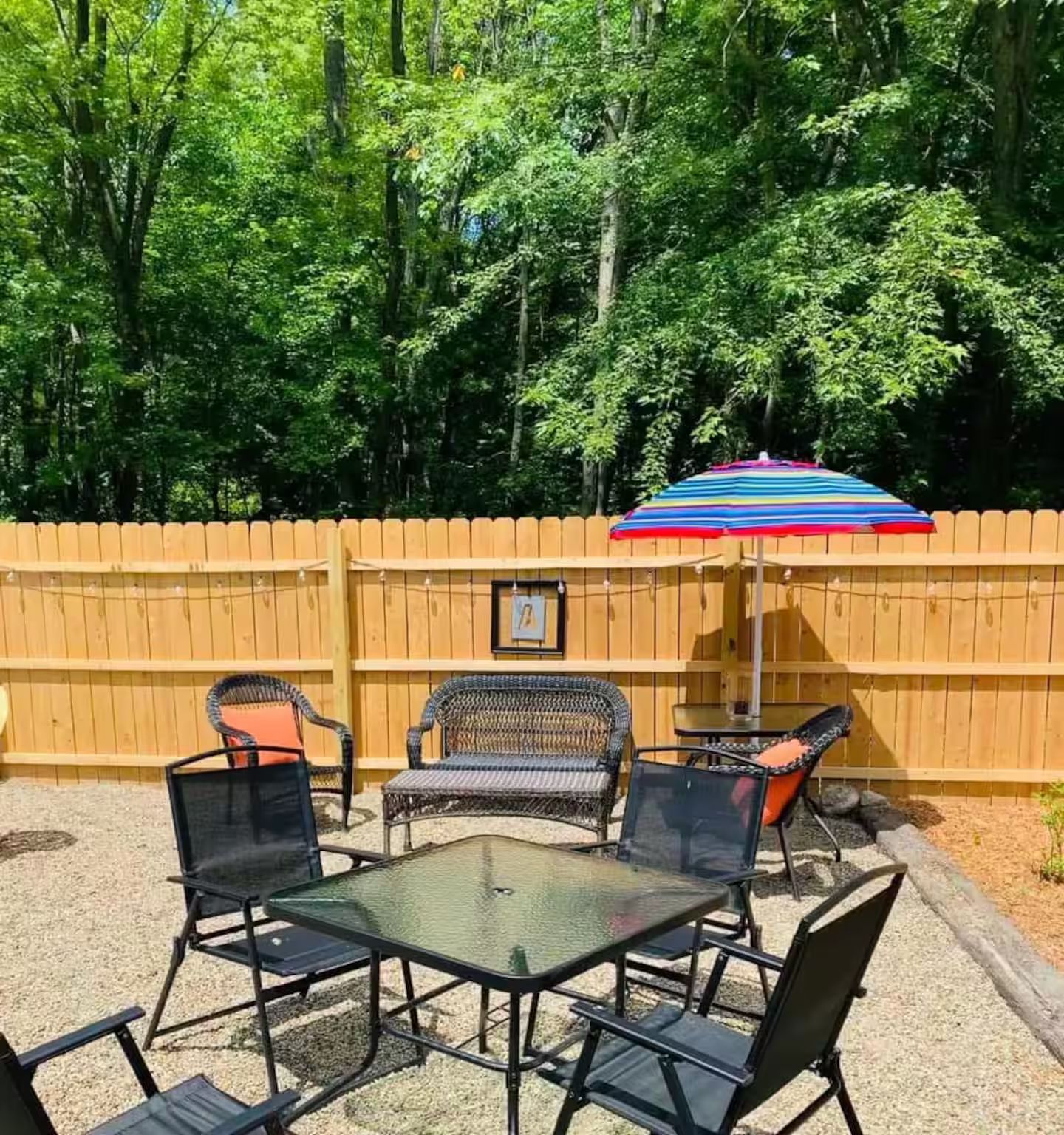 Une terrasse extérieure avec une table et des chaises, un parasol coloré et une clôture en bois.