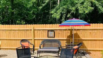 Une terrasse extérieure avec une table et des chaises, un parasol coloré et une clôture en bois.