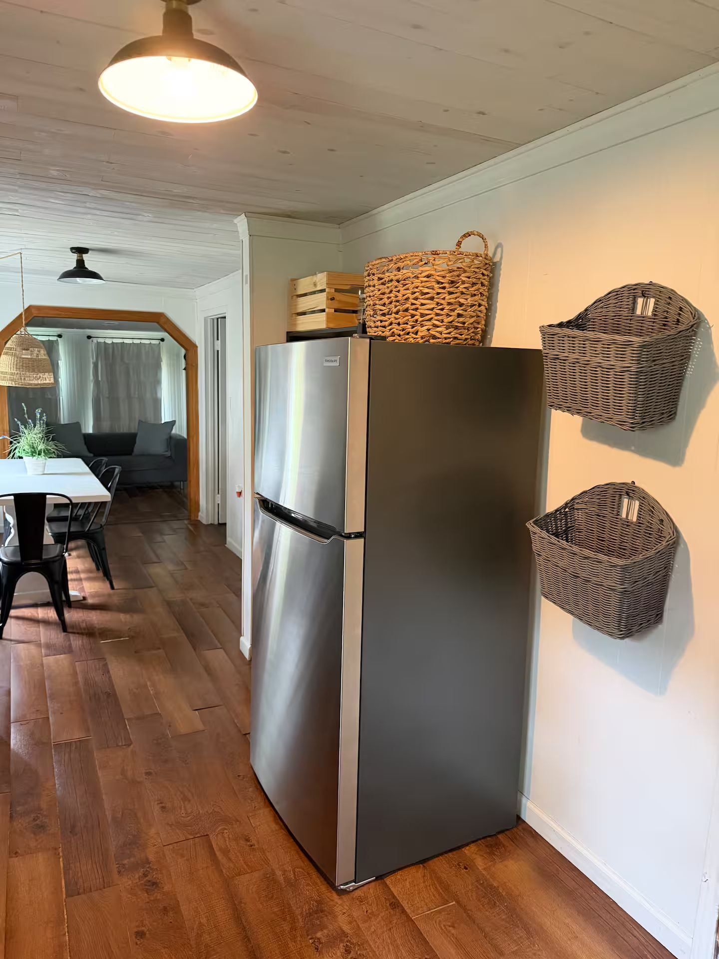 A kitchen with a stainless steel refrigerator, wooden flooring, and wicker baskets on the wall.