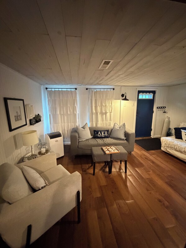 Un salón con sofá, reposapiés y una mesita con una bandeja de galletas. Se observa una puerta con ventana y una lámpara de pared.
