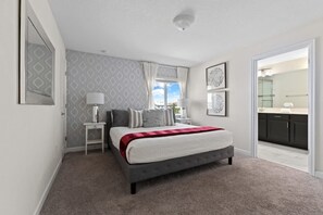 A bedroom with a bed, bedside tables, a window, and a view of a bathroom. - 5BR Home w/ Private Pool - Storey Lake Resort (Kissimmee)