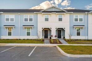 A two-story building with a symmetrical facade, featuring a central entrance with a small porch and two garage doors. - Themed 5BR Home + Pool at Windsor Cay (Clermont)